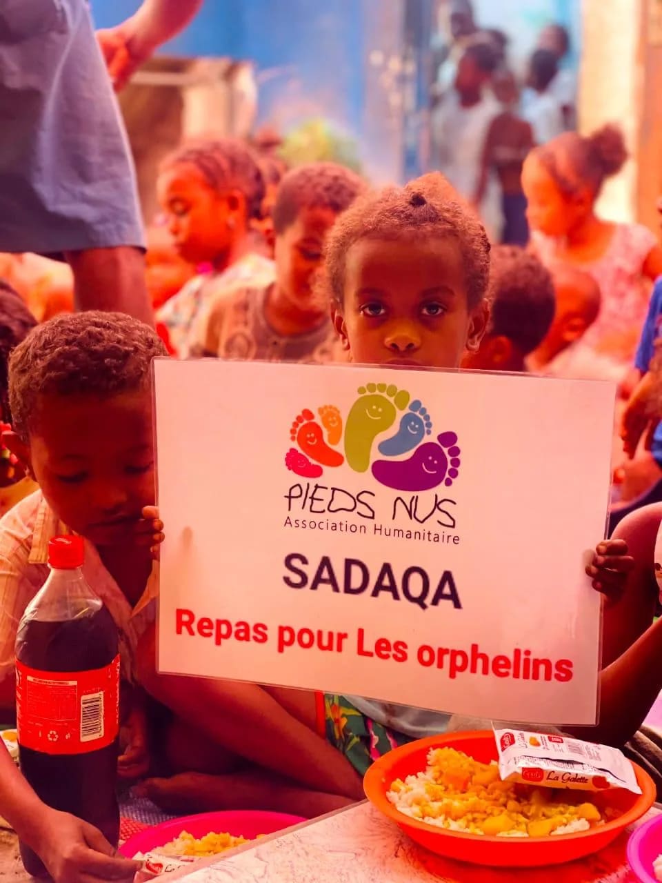 Un enfant tient le panneau « Sadaqa, repas pour les orphelins » devant son assiette de riz