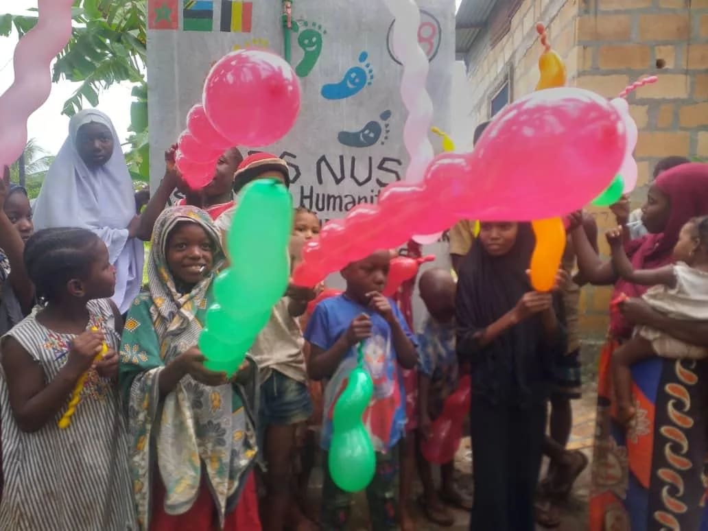 Enfants et adultes avec des ballons devant un point d'eau Pieds Nus à Zanzibar