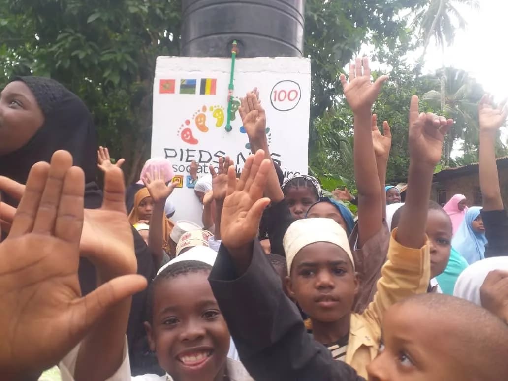 Des enfants lèvent la main, tout sourire, devant le point d'eau n° 100 à Zanzibar