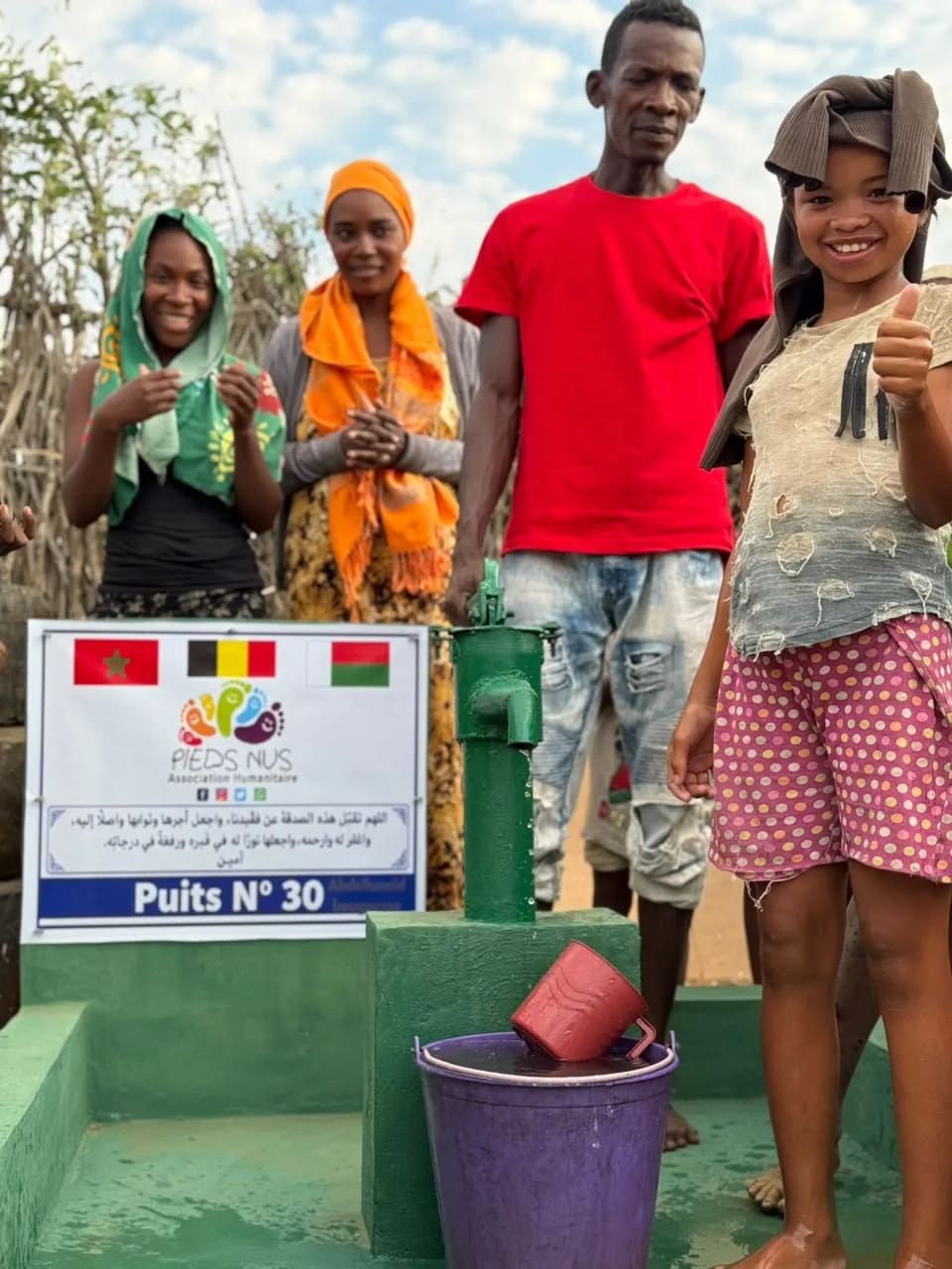A young girl giving a thumbs-up at well no. 30, next to a man in a red T-shirt