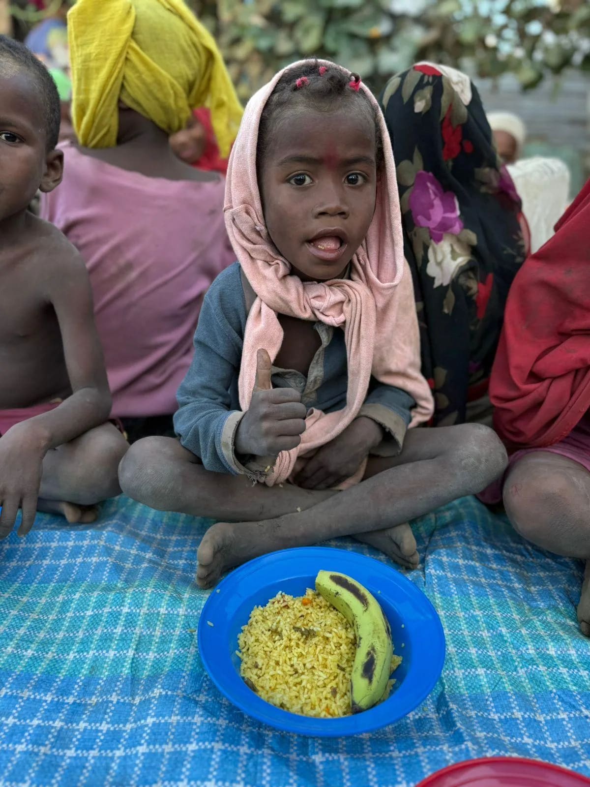 Une petite fille assise devant son assiette de riz, parmi d'autres enfants