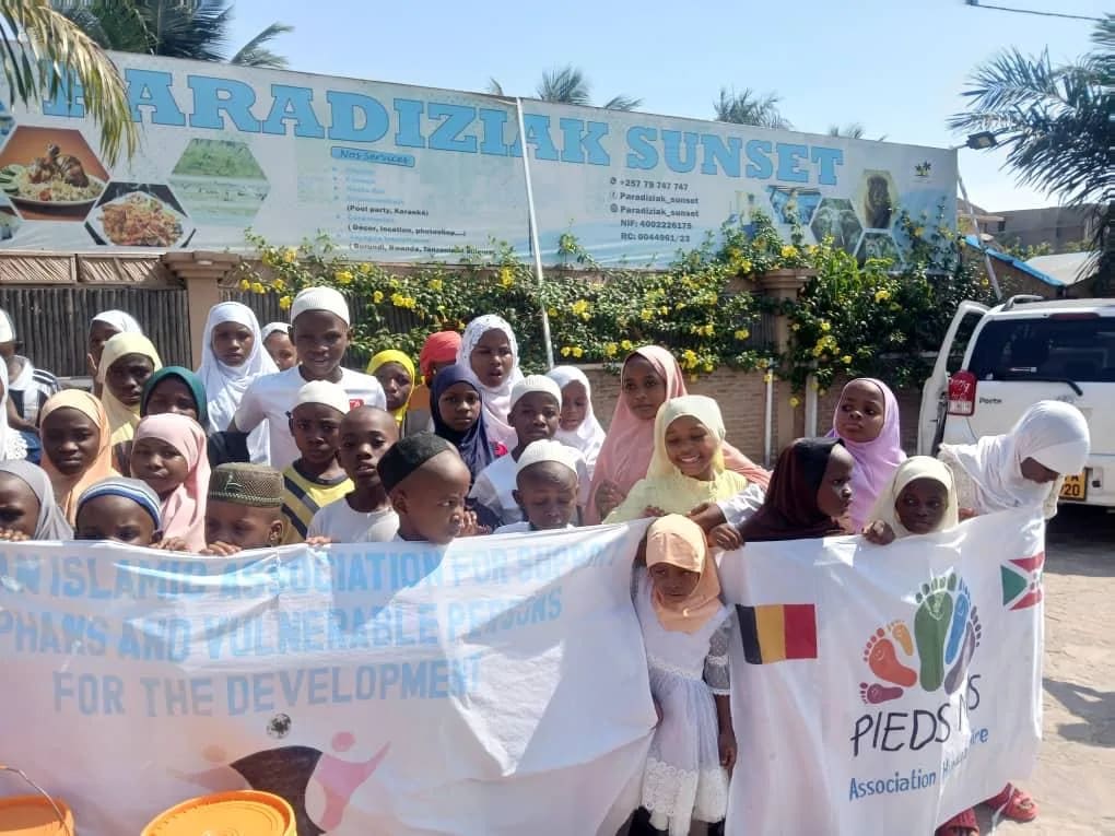 Groupe d'enfants et d'adultes derrière une bannière Pieds Nus aux drapeaux du Burundi et de la Belgique