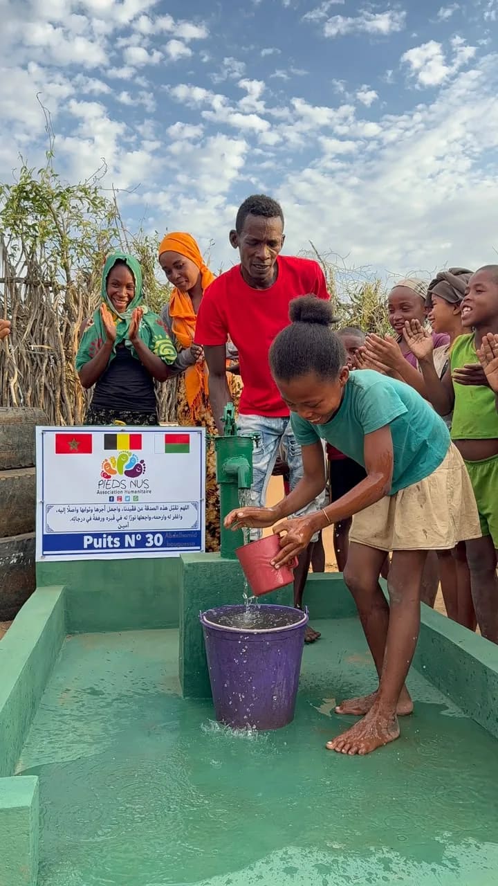 A girl filling a bucket at well no. 30, surrounded by the villagers
