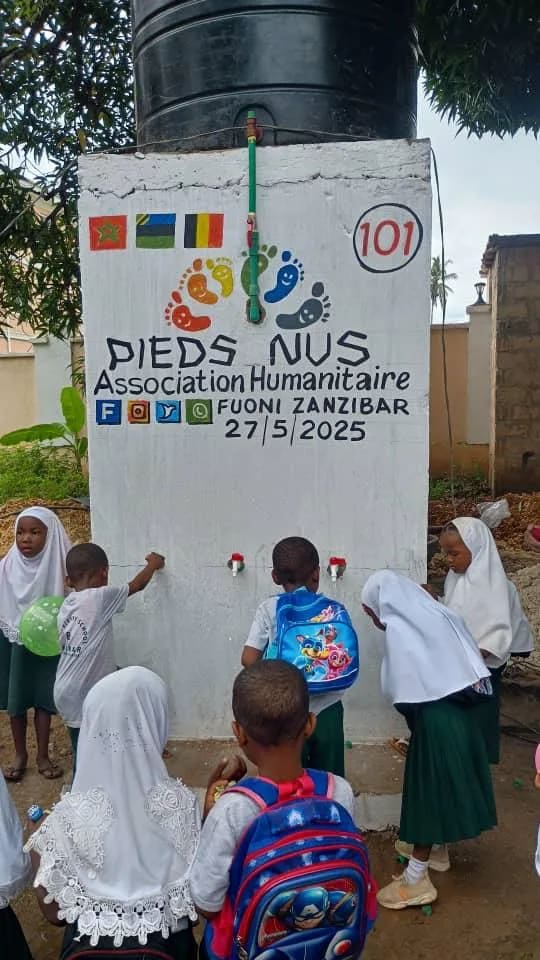 Écoliers en uniforme et cartable devant les robinets du point d'eau n° 101 à Fuoni, Zanzibar