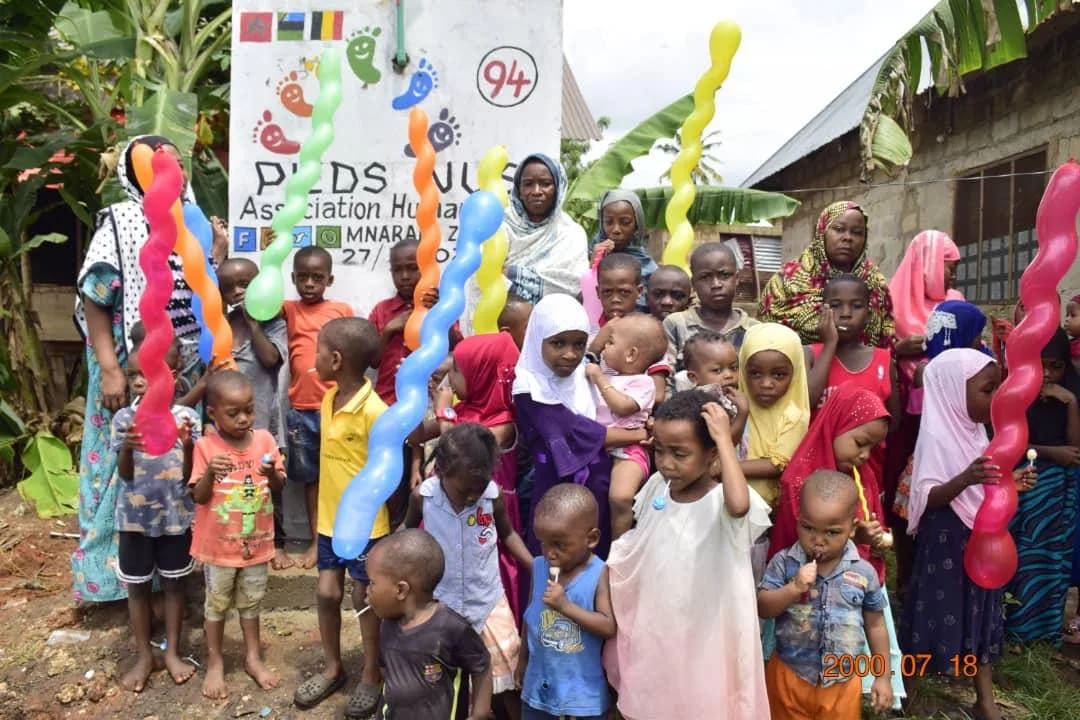 Een menigte kinderen en bewoners voor waterpunt nr. 94 op Zanzibar, met kleurrijke ballonnen