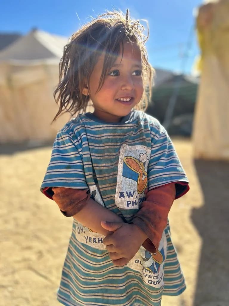 Une petite fille souriante, bras croisés, devant des tentes dans l'Atlas