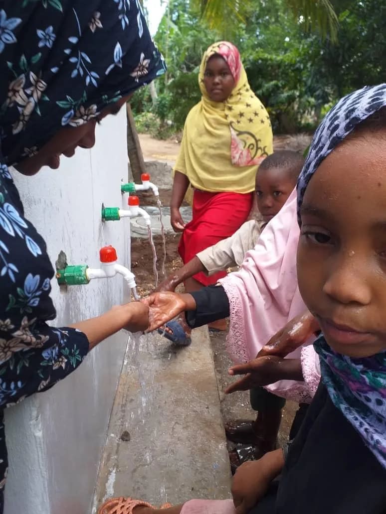 Des mains d'enfants sous l'eau qui coule des robinets du point d'eau, à Zanzibar