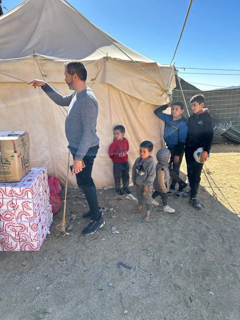 Un membre de l'équipe devant une tente dans l'Atlas, avec des enfants et des cartons de dons