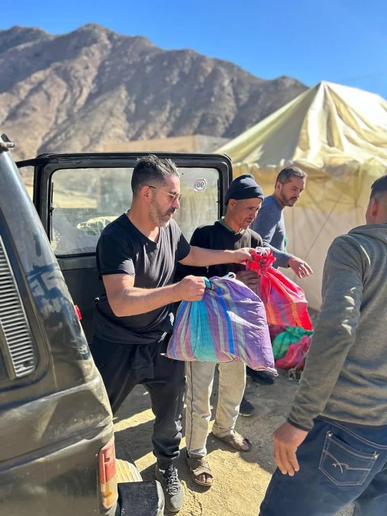 Teamleden halen zakken met hulp uit de kofferbak van een auto, aan de voet van het Atlasgebergte