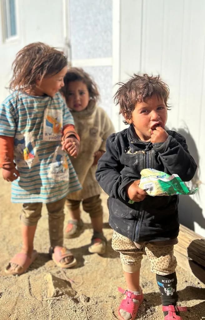 Trois jeunes enfants devant un logement préfabriqué blanc, dans l'Atlas